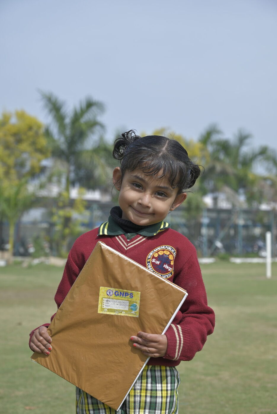 A young GNPS student smiles on the school lawn, holding her project folder