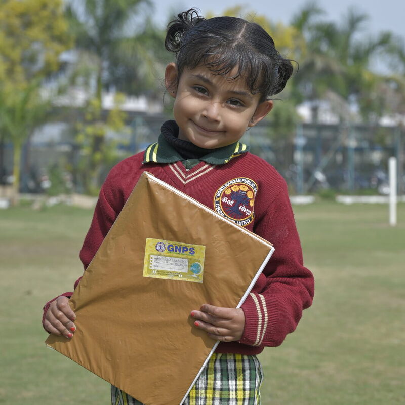 A young student smiles on the school lawn, holding her project folder